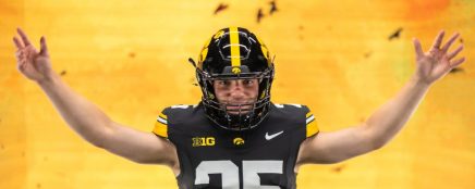 An American football player wearing a black and yellow jersey with the number 25 stands with arms outstretched against a vibrant yellow background.
