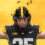 An American football player wearing a black and yellow jersey with the number 25 stands with arms outstretched against a vibrant yellow background.