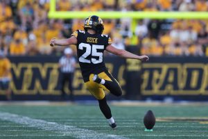 A football player wearing a black and yellow uniform with the number 25 kicks a ball during a game.