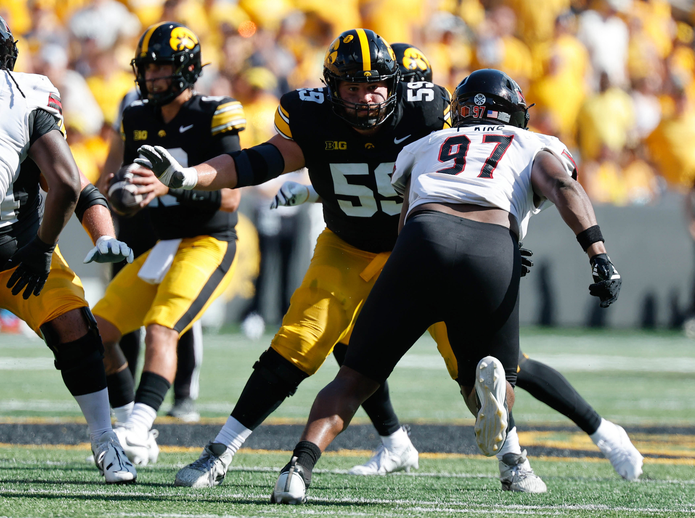A football player in a black and yellow uniform with the number 55 is engaged in a play, facing off against an opponent wearing number 97 on a white jersey.
